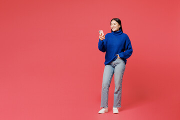 Full body young woman of Asian ethnicity she wearing blue sweater casual clothes hold in hand use mobile cell phone chatting online isolated on plain pastel pink background studio. Lifestyle concept.