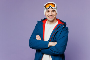 Skier happy smiling man wear warm blue windbreaker jacket ski goggles mask hold hands crossed folded spend extreme weekend winter season in mountains isolated on plain purple background Hobby concept