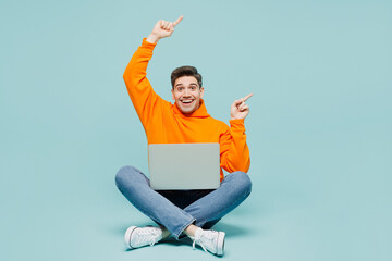 Full body young IT man wearing orange hoody casual clothes sitting hold use work on laptop pc...