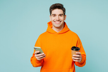 Young man wear orange hoody casual clothes hold takeaway delivery craft paper brown cup coffee to...