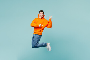 Full body young amazed man he wears orange hoody casual clothes jump high point index finger aside...