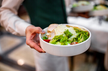 Men's waiter hands hold a Caesar salad 