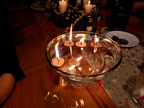 a traditional Christmas table with a metal tree and candles spins the merry-go-round with hot air. tinkling carillon. dropping a candle shell in a bowl of water is a tradition