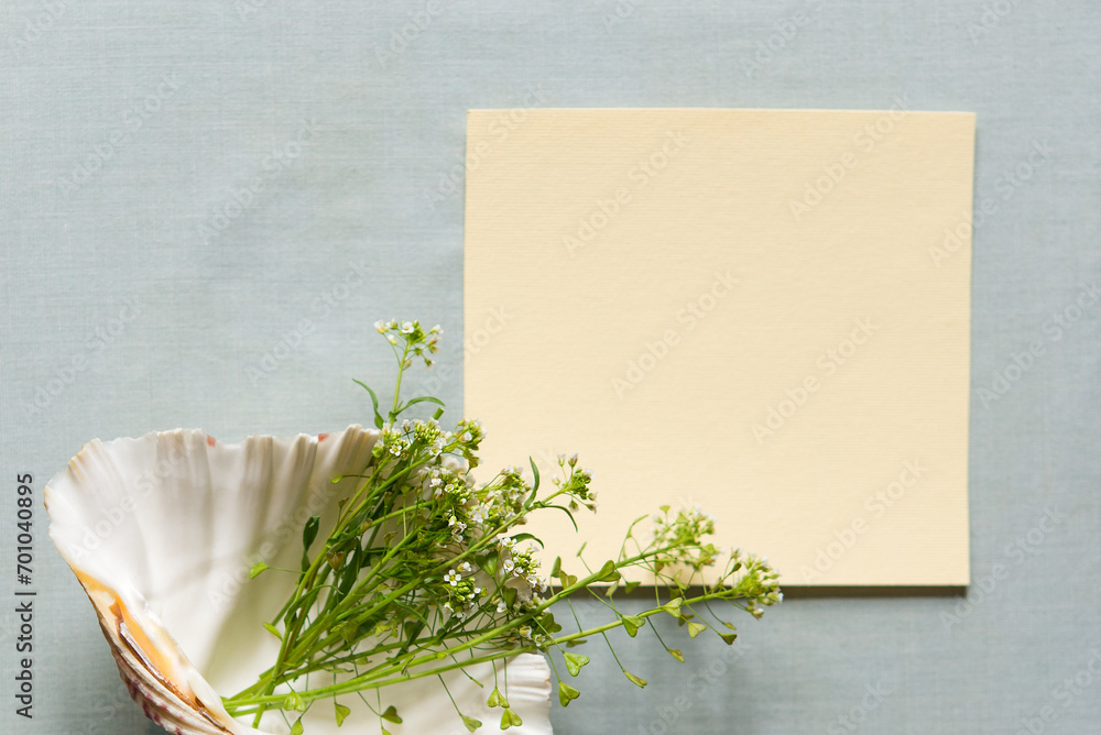 Wall mural Light empty sheet of paper mockup. Green branches with white inflorescences on a shell on a textile background. Blank greeting card mockup. Flat lay. Happy Mother's Day and Women's Day.