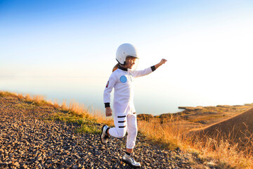 Astronaut futuristic kid girl with white full length uniform and helmet wearing silver shoes outdoors