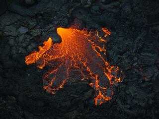 Unique view of molten lava flow burning and slowly moving down rugged volcanic rocks terrain, aerial close up shot. Volcano eruption and natural disaster concepts. - obrazy, fototapety, plakaty