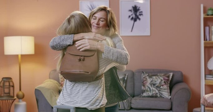 Happy woman, suitcase and hug mother for visit, greeting or welcome home from travel in living room, care or support. Mom hugging young female person or daughter with luggage for embrace at house