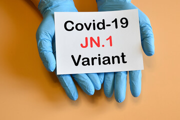the doctor's hands hold a paper with text 'Covid-19 JN.1 Variant'.