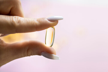 Young female hands are holding yellow omega 3 gel capsule close-up. Fish oil supplement. The...