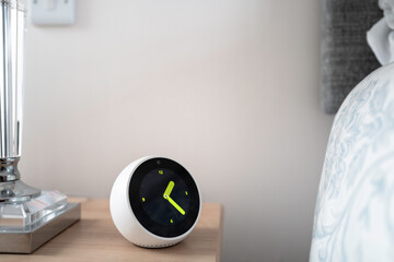 Smart assistant device showing the analog time located on a bedside table. Part of a large glass...