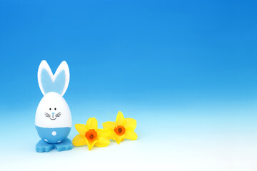 Easter bunny rabbit blue egg with Spring narcissus flowers on gradient blue white background....
