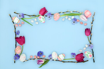Easter background border with edible and decorative eggs, flowers and willow branch on pastel blue....