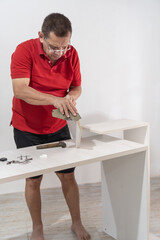 Senior Man in red shirt using saw on furniture piece, deeply involved in DIY crafting.