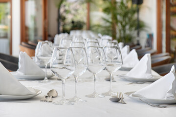 Table arrangement with polished cutlery on each side of elegant crookery, complemented by a cone-shaped cotton napkin, setup for a three-course meal symmetrically aligned with wine and water glasses
