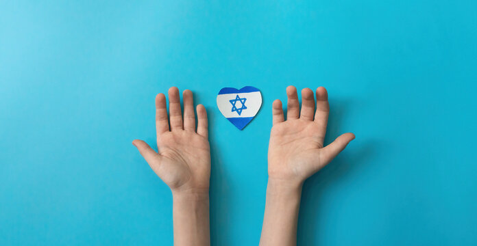 children of Israel with love for their native country. child's hands and a paper-cut drawn Israeli flag in the shape of a heart on a blue background.