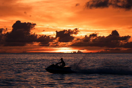 Paynes Bay Beach, Barbados: an amazing colorful sunset in the caribbean sea with the silhouette of a jet ski in the foreground.
