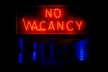 neon no vacancy sign at night in front of motel with blue lights