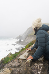 Unknown woman with a knit hat an jacket spotting an exceptional view of a wild beach on the Irish...