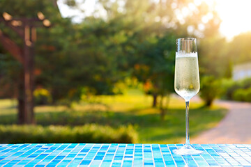 Elegant flute glass of sparkling white wine or champagne by side of swimming pool