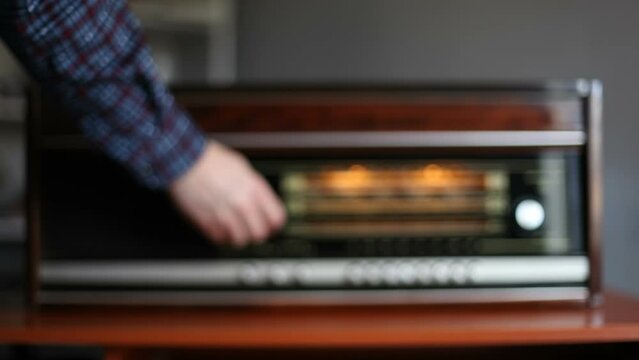 A man turns on a retro radio and searches for a radio wave. Blurred video.