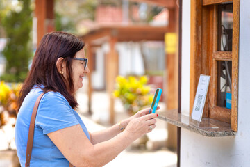 Woman scans a QR Code on the display of a street-side eatery using her smartphone, illustrating...