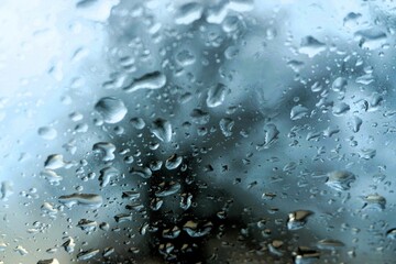Abstraktes Motiv mit Wassertropfen auf Glasscheibe vor Baum und blau-grauem Himmel bei Regen am Nachmittag im Winter