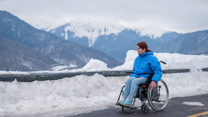 Caucasian woman in a wheelchair travels in the mountains in winter. - obrazy, fototapety, plakaty