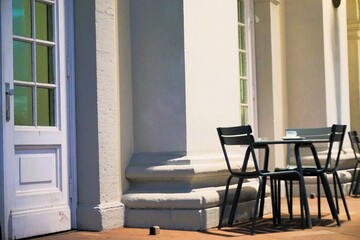 Terrassencafé mit Stühlen und rundem Tisch vor weißen Wänden von herrschaftlichem Gebäude am Abend im Winter