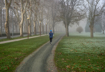 an athlete runs in the park on a foggy winter morning