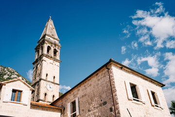 Fototapeta na wymiar Old stone house with white shutters and an attic against the backdrop of the bell tower of the Church of St. Nicholas. Perast, Montenegro