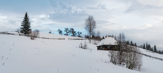 Countryside hills, groves and farmlands in winter remote alpine mountain village, and small old abandoned house on hillside