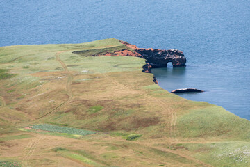 vue sur un bout de terre recouvert de gazon vert au bord de l'eau avec des falaises de roche rouge