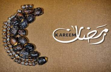 Date fruits and rosary moslim arranged in moon shape on a straw plate. Islamic festive food and...