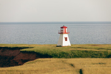 Fototapeta na wymiar vue sur un phare blanc et rouge en été au bod de la mer avec du gazon vert lors d'une journée ensoleillée