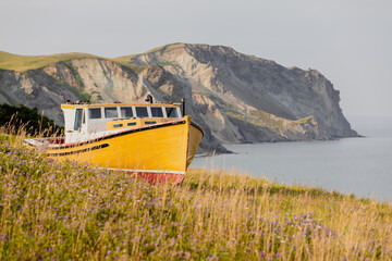 vue sur un bateau peint en jaune et blanc au bord de la mer avec des falaises en arrière plan en...