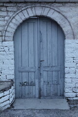 Old grayish-blue, double leaf, round arch wood door cut into a stone wall, old town upper part. Gjirokaster-Albania-187