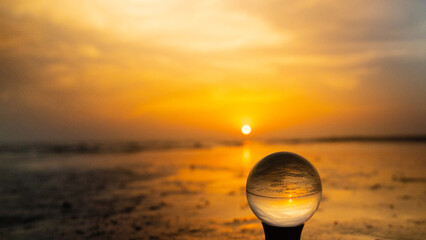 Colorful yellow, orange sunrise at the beach, reflected in surf and crystal lens ball on a stand....