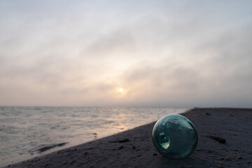 Obraz premium Cloudy sunrise over beach with hand-blown glass float for fisherman's net resting in the sand 