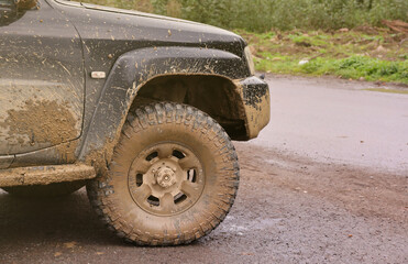 Wheel closeup in a countryside landscape with a mud road. Off-road 4x4 suv automobile with ditry body after drive in muddy road area