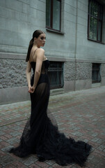 A 30-year-old girl in a black transparent revealing dress on a city street. Style and elegance, femme fatale, photo shoot, advertising, girl.Drama