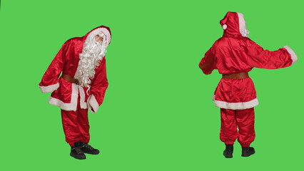 Impatient santa claus looks at time on wristwatch, trying to be punctual while he stands over full body greenscreen. Saint nick character with white beard spreading christmas spirit.