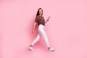Fototapeta na wymiar Full length photo of walking business lady make a blog in social networks working remotely using phone isolated on pink color background