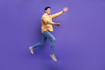 Fototapeta na wymiar Full size photo of attractive young man running stretch hands want hug dressed stylish yellow clothes isolated on purple color background
