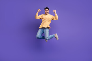 Obraz premium Full size photo of attractive young man jumping raise fists celebration dressed stylish yellow clothes isolated on purple color background