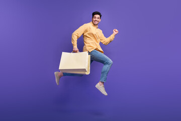 Full size photo of attractive young man running fast hold shopping bags wear trendy yellow clothes...