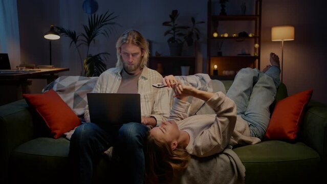 Married couple in living room using smartphone and laptop