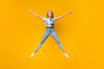 Fototapeta na wymiar Full length photo of good mood funky woman wear print stylish blouse denim pants jumping like star isolated on yellow color background