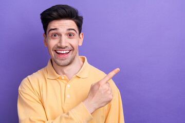 Photo of positive excited guy wear yellow polo pointing finger empty space isolated violet color background