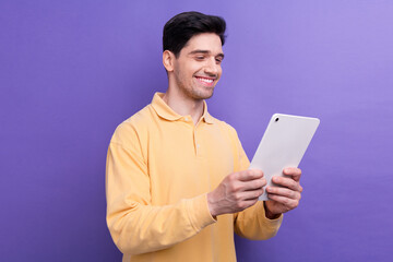 Photo of cheerful attractive man dressed yellow shirt reading news modern device isolated purple color background
