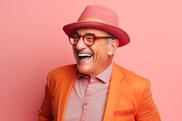 Portrait of happy senior man in orange suit and hat laughing and looking at camera isolated over pink background